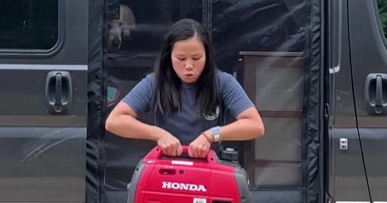 Woman lifting a portable Honda generator out of a camper van on a cloudy day